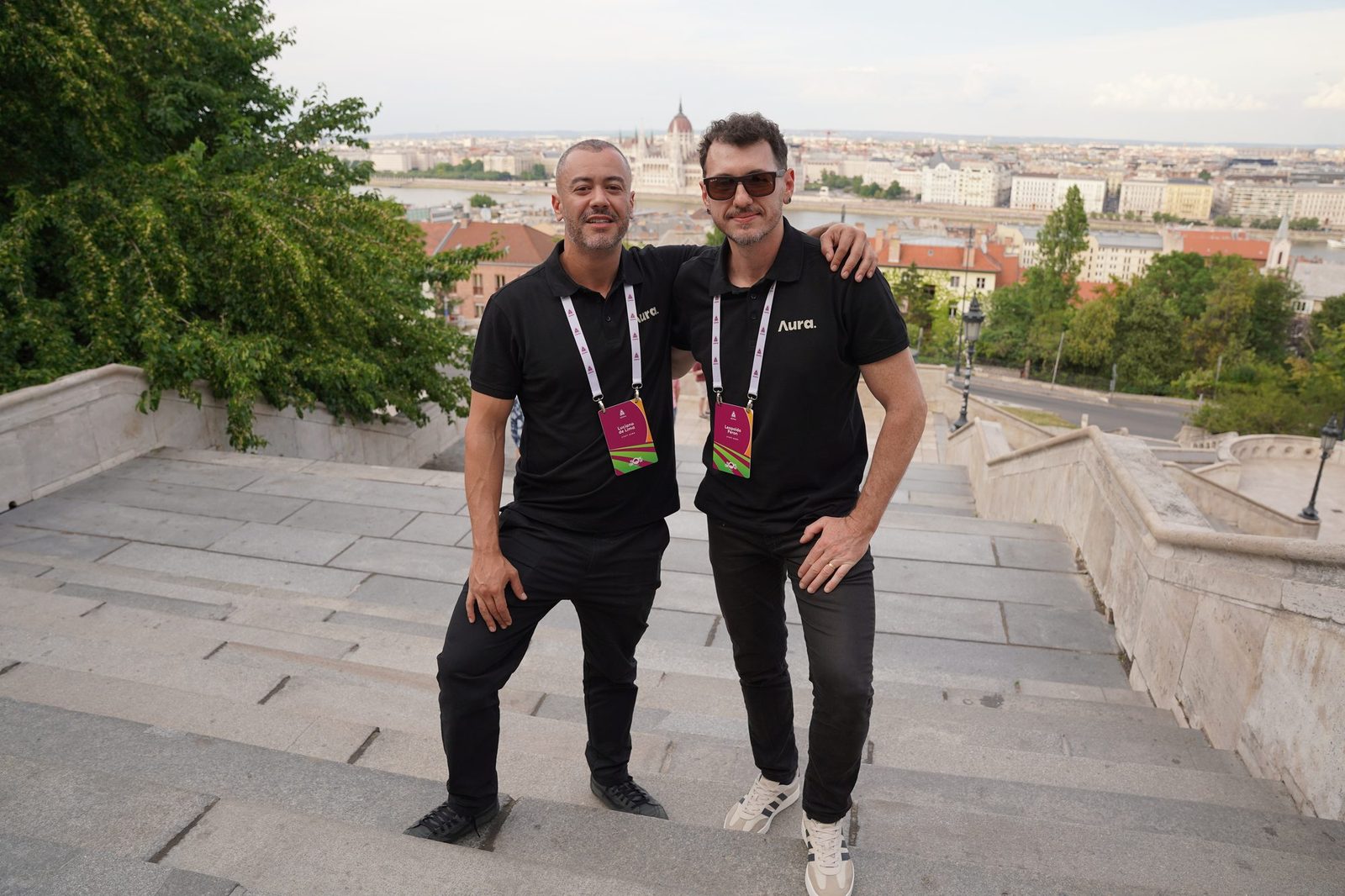 Now We Grow, Budapeste 2026: dois integrantes da equipe posando em uma escadaria, com a cidade ao fundo