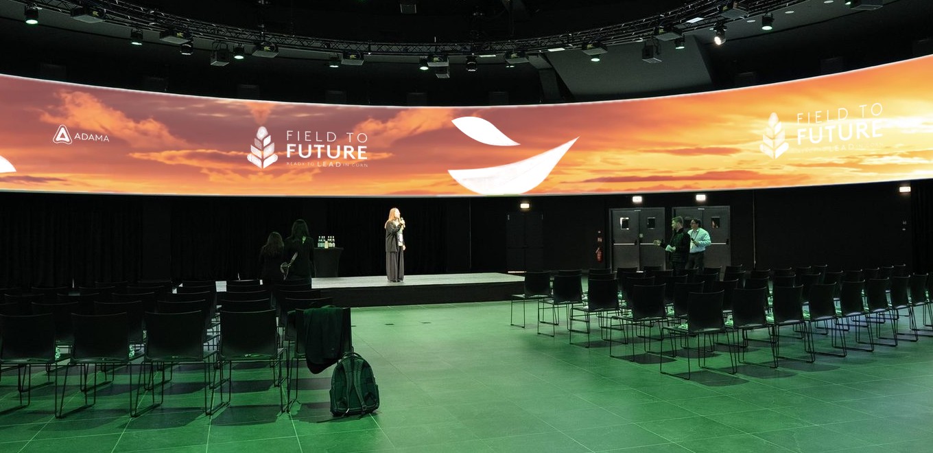 Frame de ADAMA Global: sala 360° com a tela do evento Field to Future