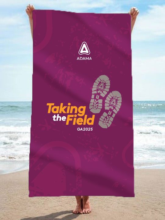 Take The Field, Pafos 2025: toalha de praia roxa com a marca Taking the Field, aberta na praia