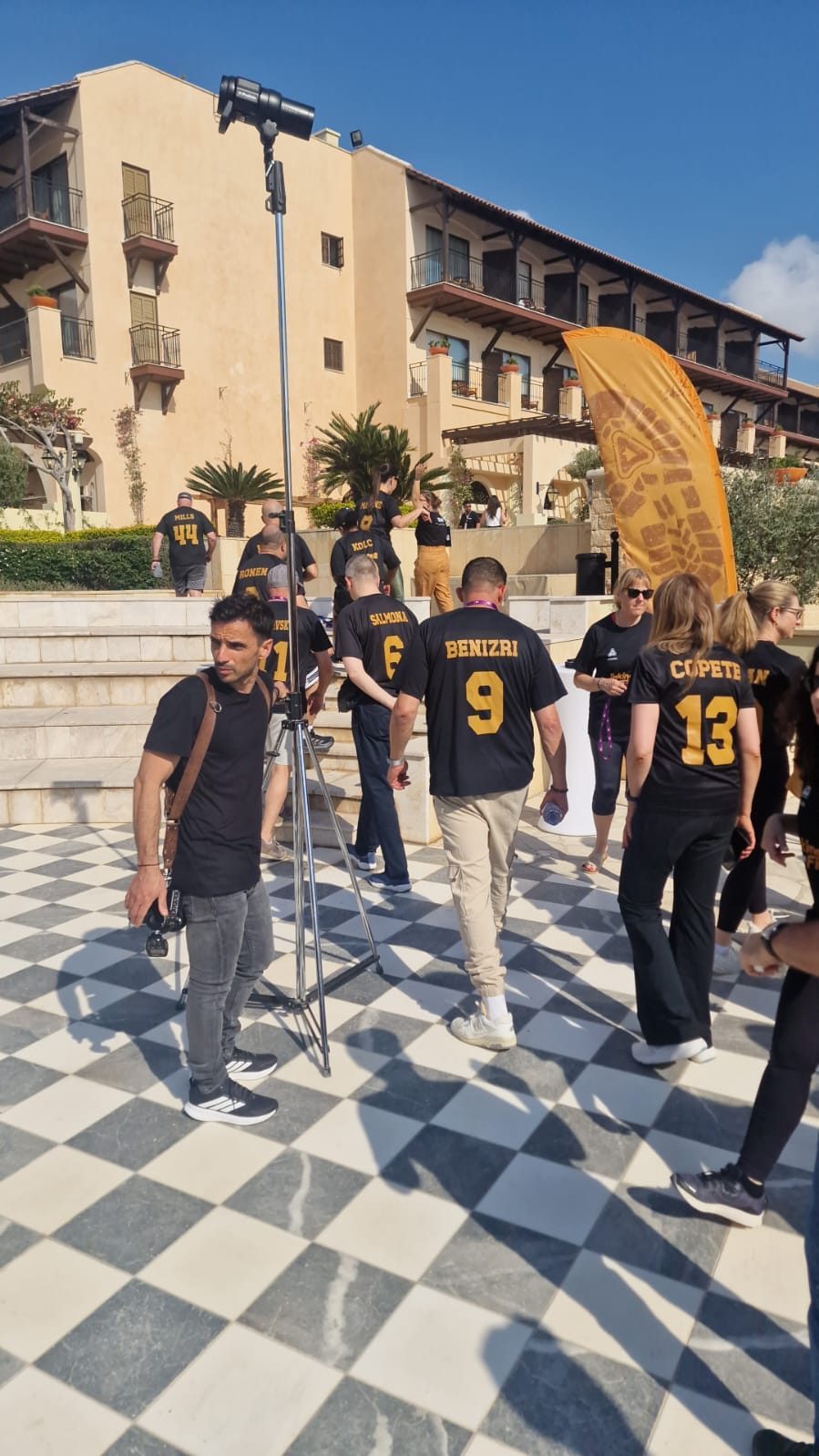 Take The Field, Pafos 2025: participantes de camisas pretas em um pátio de piso xadrez