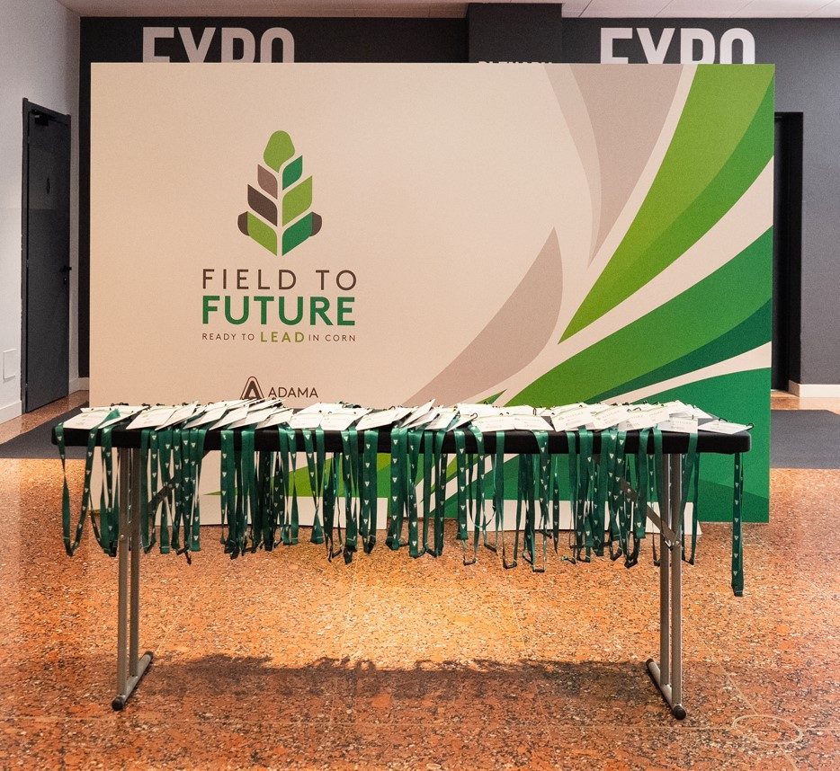 Field to Future, Milão 2026: backdrop Field to Future e mesa com credenciais e cordões verdes
