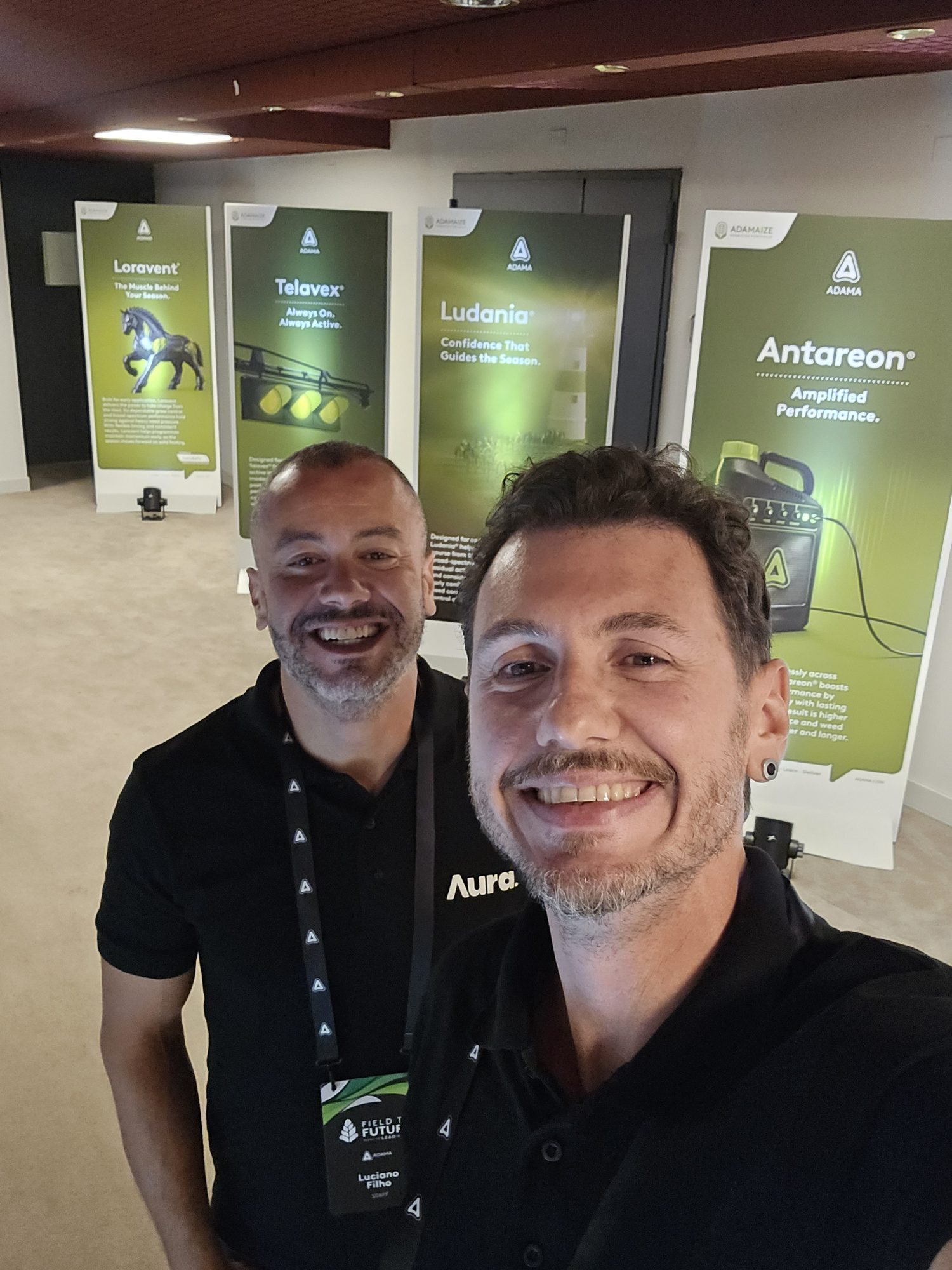 Field to Future, Milão 2026: selfie de dois integrantes da equipe diante de painéis de produtos