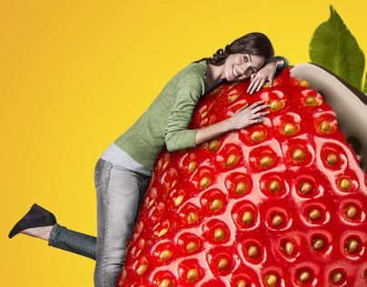 Nutri-frutas: mulher abraçando um morango gigante sobre fundo amarelo